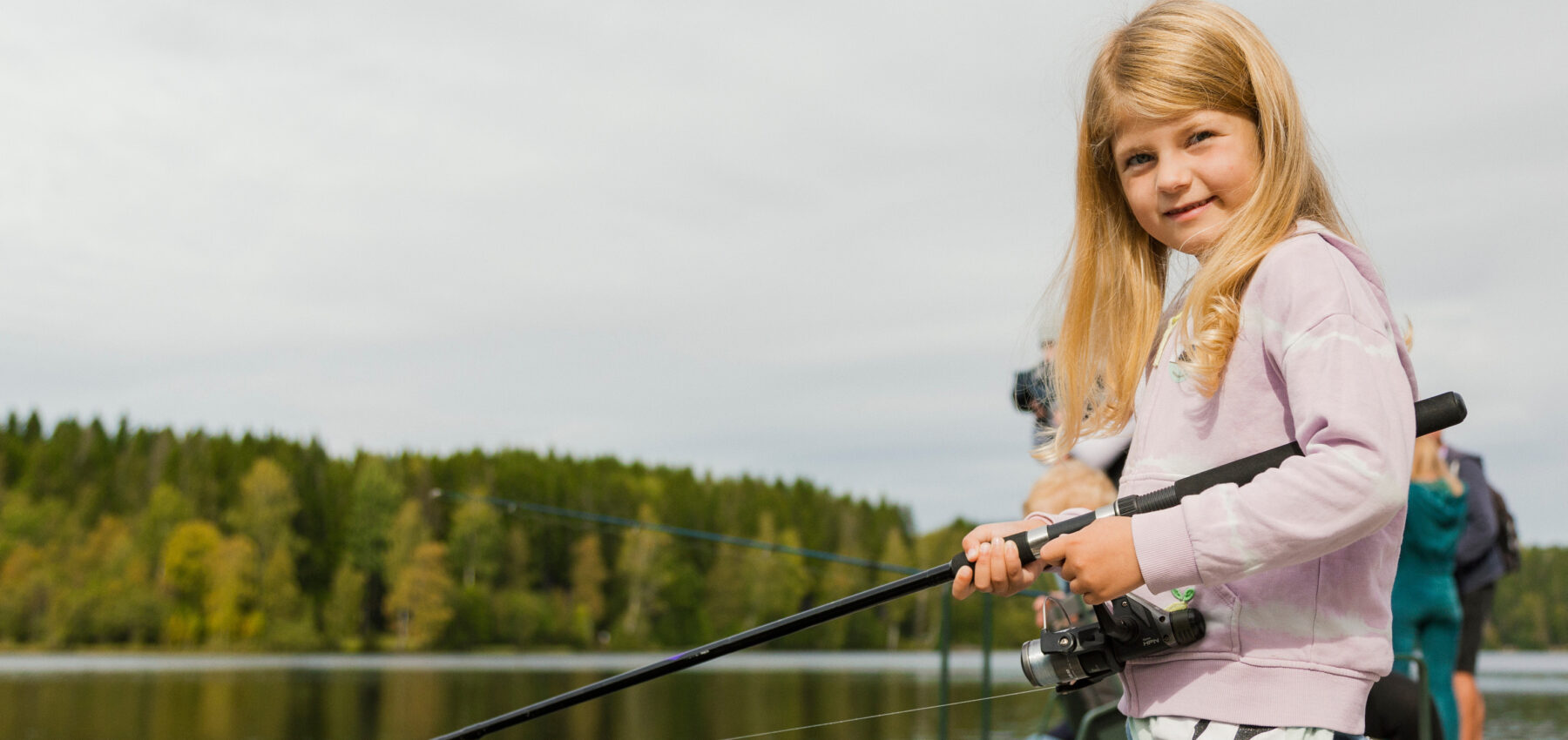 Jente som strå ved et vann og holder en fiskestang