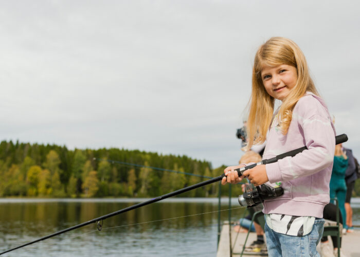 Jente som strå ved et vann og holder en fiskestang