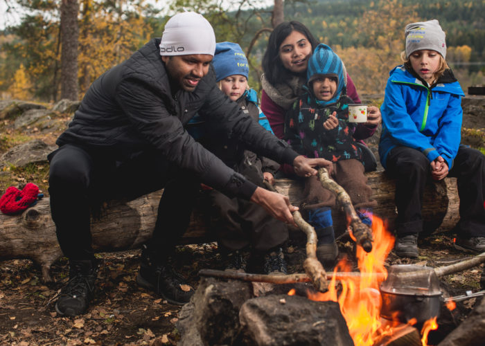 Two adults and three kids preparing food over fire, at a campsite.