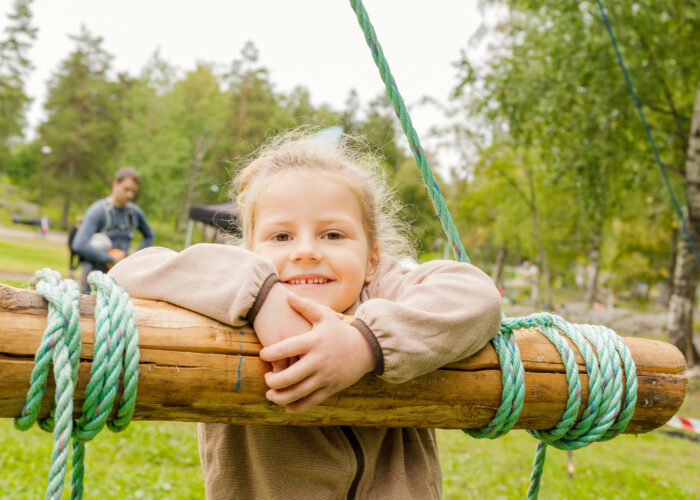 Jente som smiler og lener seg på en speiderkarusell.