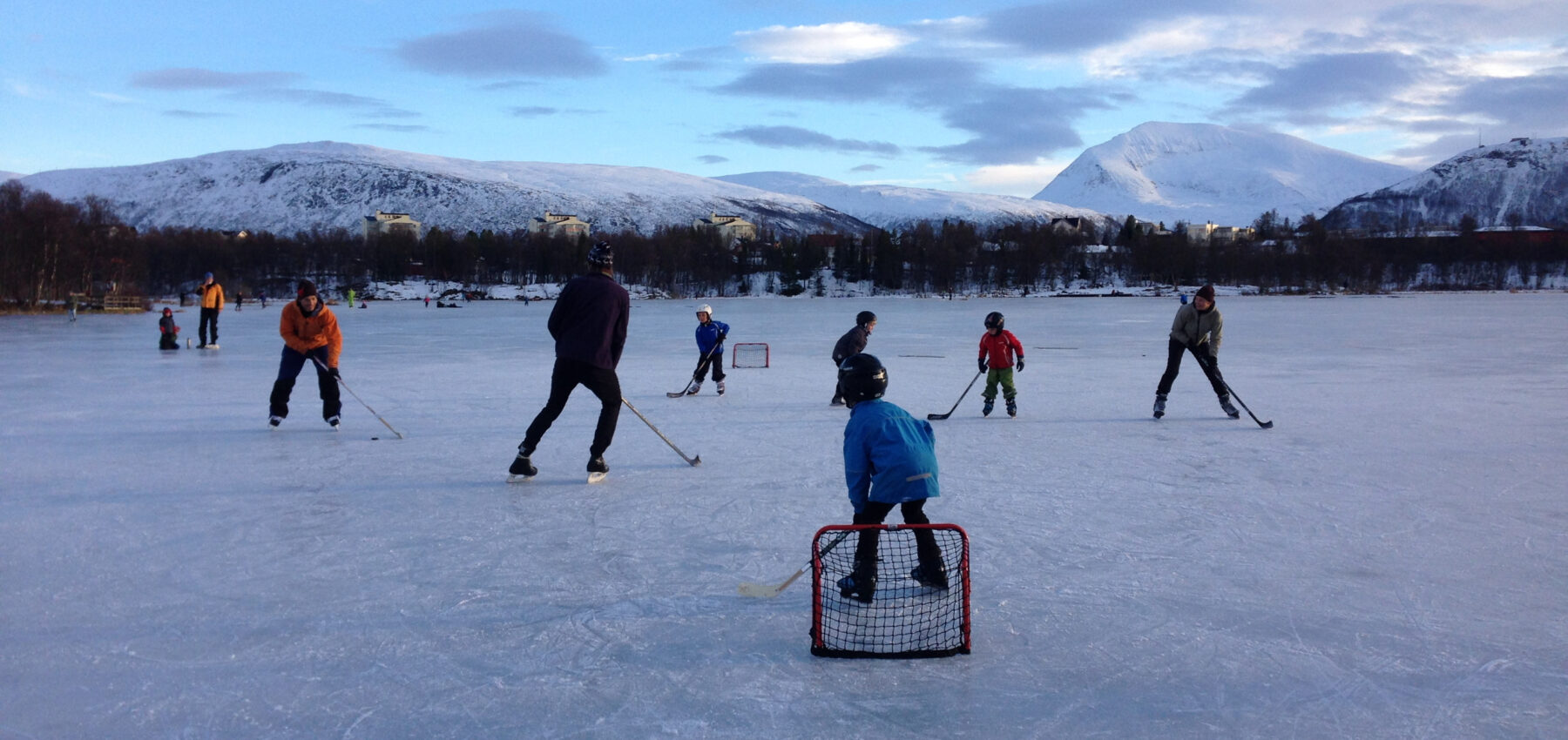 Barn og voksne spiller ishockey ute på et vann