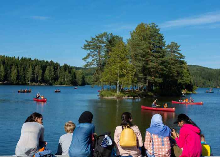 En gruppe sitter ved vannkanten og ser på barn som padler i kano på Sognsvann.