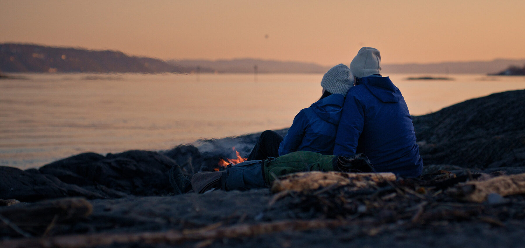 Et par sitter og ser ut over fjorden etter solnedgang.