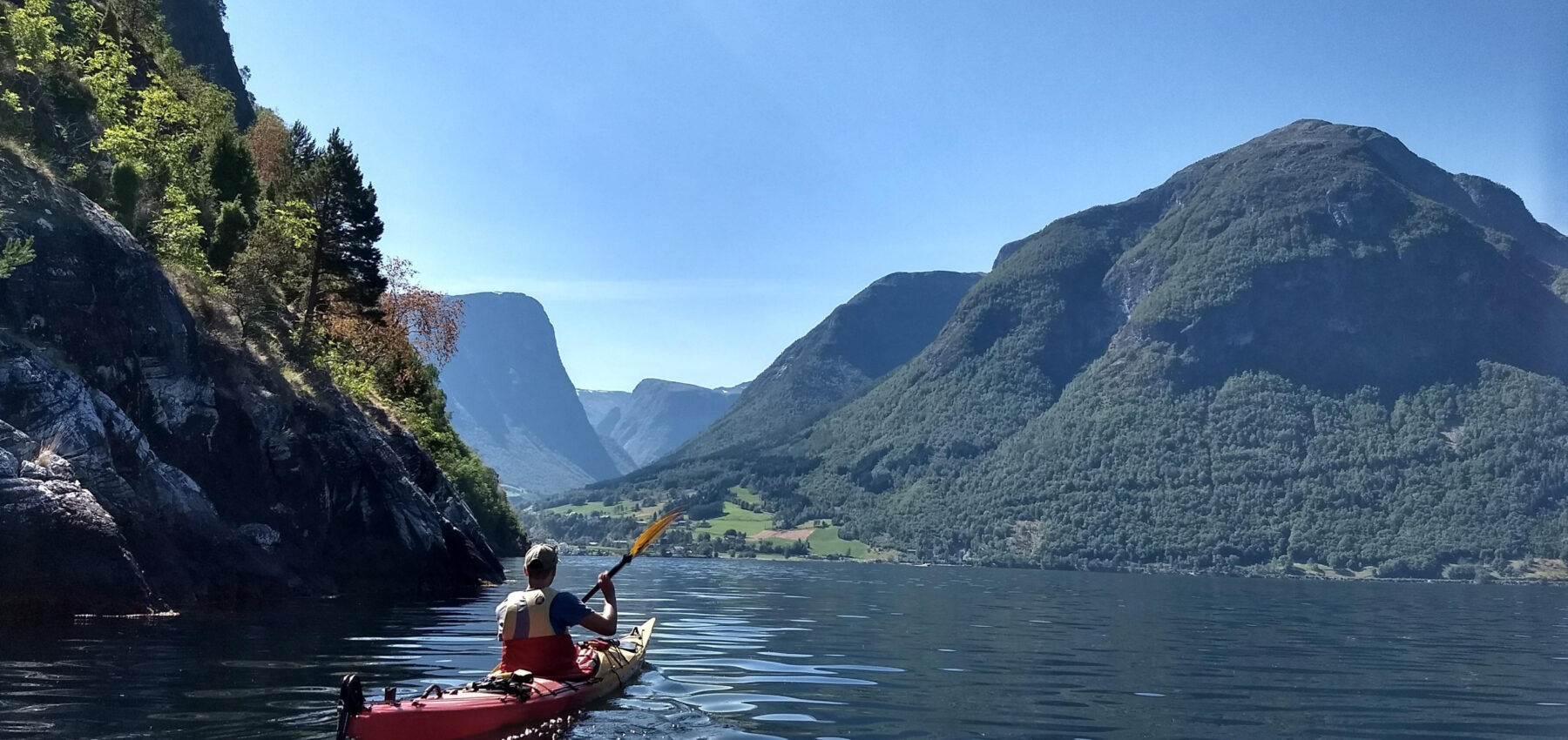 To personer padler i fjorden mellom ruvende fjell