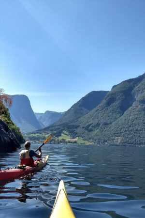 To personer padler i fjorden mellom ruvende fjell