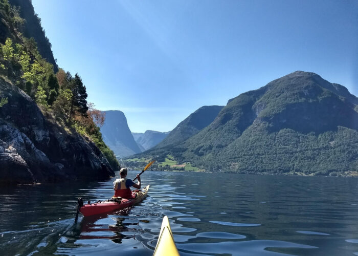 To personer padler i fjorden mellom ruvende fjell